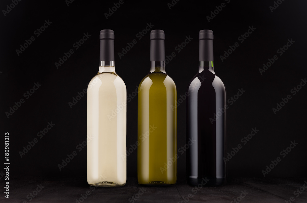 Wine bottles set - red, green, white - mock up on elegant dark black wooden background.