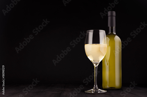 Green bottle of white wine and wine glass mock up on elegant dark black wooden background, copy space.