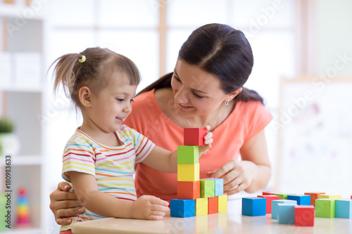 Cute woman and kid playing educational toys at kindergarten or nursery room