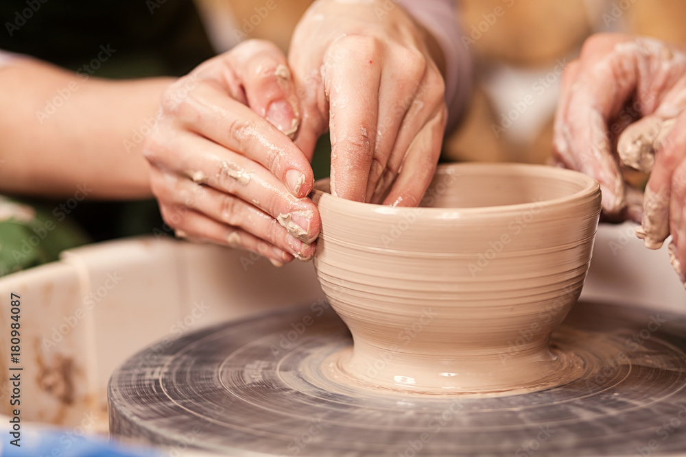 A close-up of the woman's potter teaches the pupil how to make a deep bowl of clay on a potter's wheel in the workshop