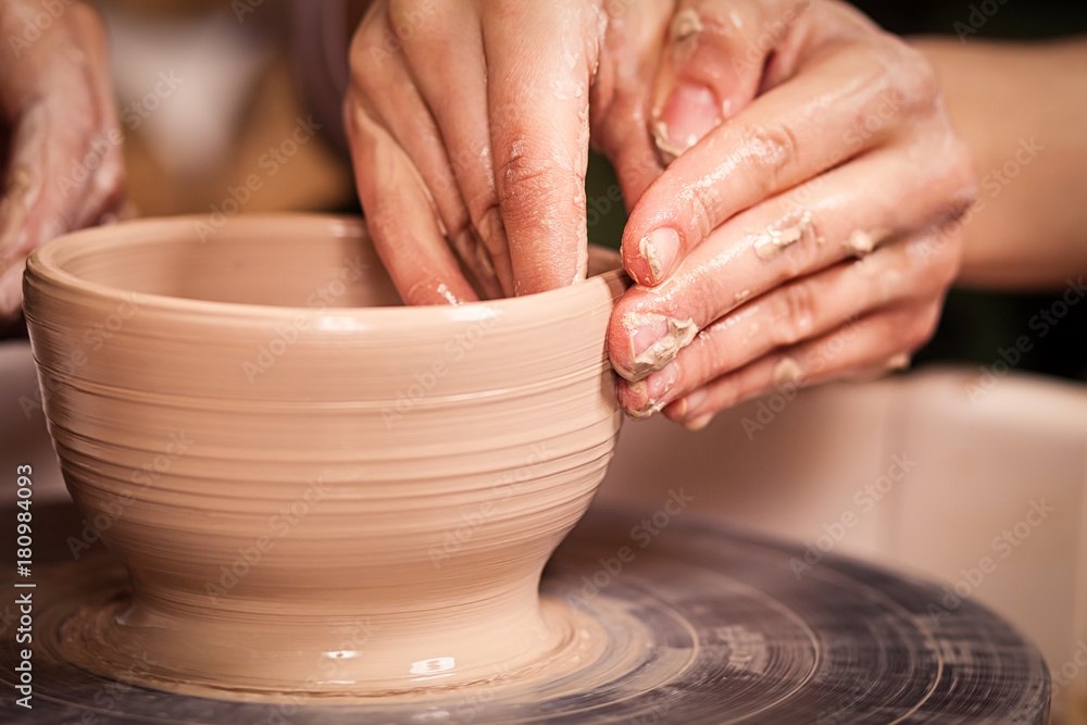 A close-up of the woman's potter teaches the pupil how to make a deep bowl of clay on a potter's wheel in the workshop A close-up of the woman's potter teaches the pupil how to make a deep bowl of clay on a potter's wheel in the workshop