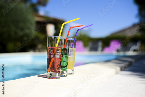 Three tropical colorful drink cocktail with straw on the poolside of resort swimming pool with nobody.