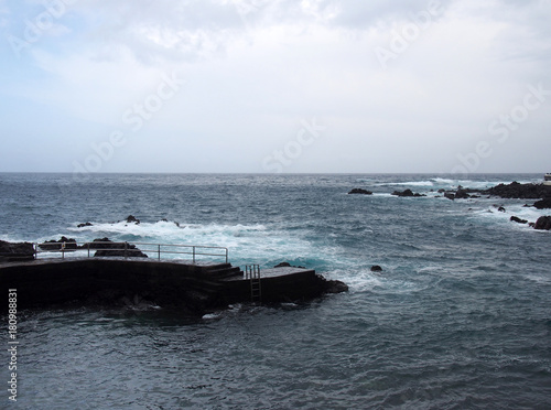 waves breaking on the historic old harbour in puerto cruz in tenerife with surf and dark sea on a winters day
