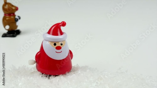 Cute Rudolph the red-nodes reindeer windup dolly walks next to a winking Santa Claus