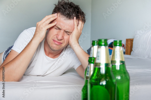 Hangover suffering man holding his aching head close up portrait with bottles of beer. Alcoholism concept. photo