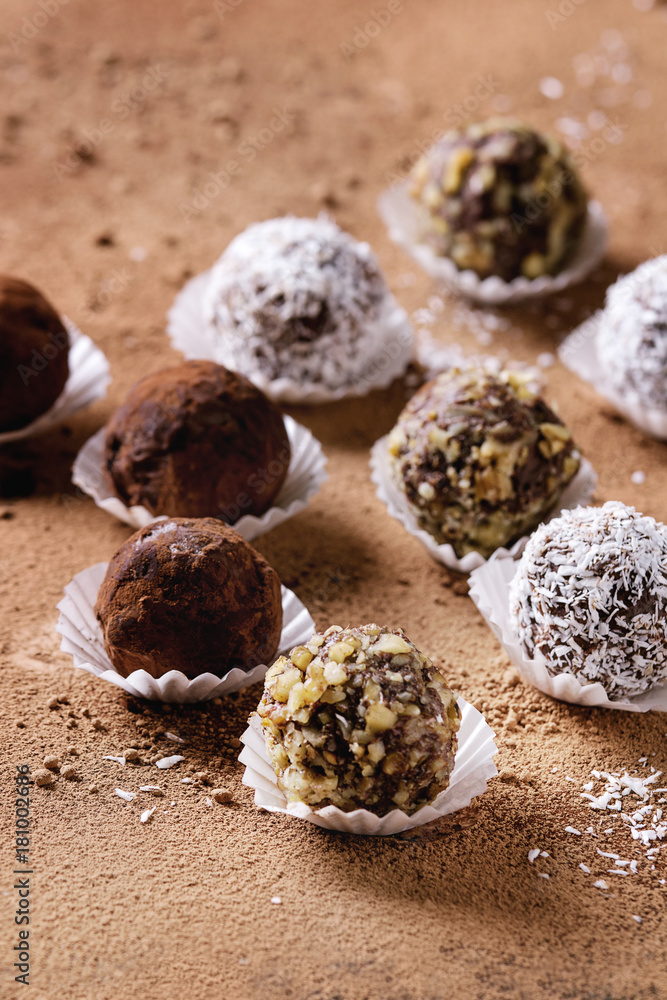 Variety of homemade dark chocolate truffles with cocoa powder, coconut, walnuts over cocoa powder as background. Close up, copy space. Variety of homemade dark chocolate truffles with cocoa powder, coconut, walnuts over cocoa powder as background. Close up, copy space.
