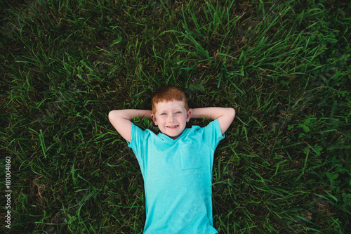 Overhead portrait of red haired boy lying on grass photo