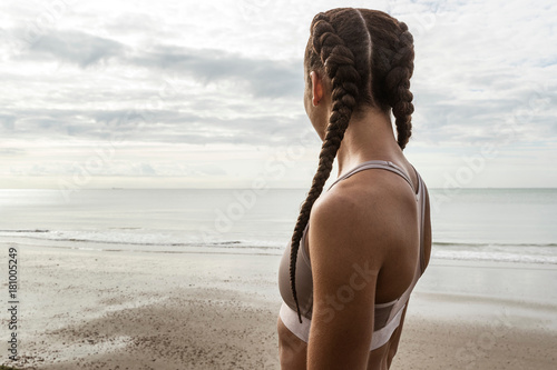 Young female runner with hair plaits looking out to sea from beach