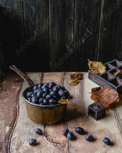 fresh plums in vintage metal pan with old keys, vintage wooden box and dry leaves on brown gradient background photo