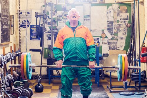 Senior male powerlifter struggling to lift barbell in gym