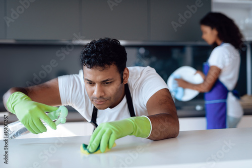 Black man and woman in the kitchen at home. They clean in the kitchen. A man washes the countertop with detergent.