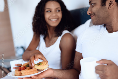Black man and woman in the bedroom. They have breakfast in bed.