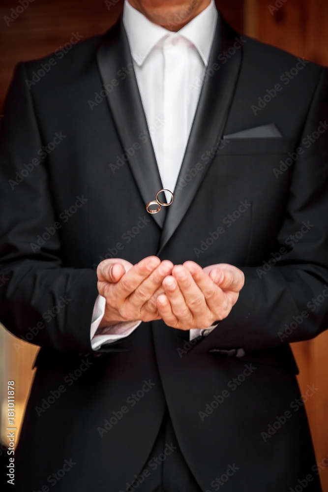 A stylish bridegroom in a black suit tosses wedding gold rings from her hands