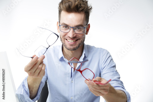 Młody, uśmiechnięty mężczyzna wybiera oprawki okularów 