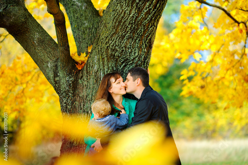 happy family strolls in an autumn park, stand and hug near a big tree with beautiful foliage.