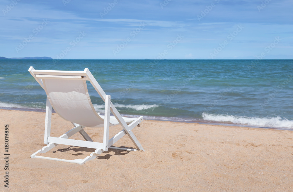 Empty white wooden beach chair on sandy tropical beach with  blue sky background