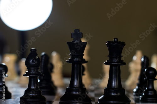 king queen and bishop close up on a chessboard and a single light above