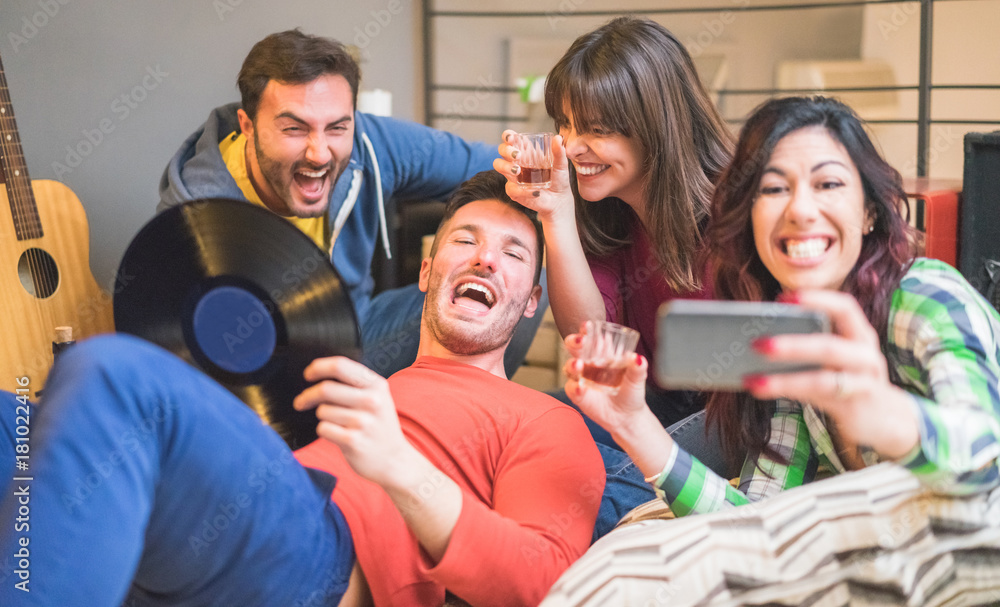 Obraz premium Happy friends taking selfie photo with smartphone camera at hostel party - Young people drinking and having fun together - Focus on left woman face - Friendship, music and gathering concept