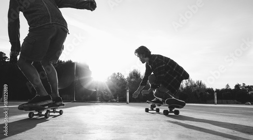 Two skaters friends training outdoor in city park at sunset - Young people skateboarding with longboard in urban contest - Extreme sport concept - Focus on right man legs feet - Vintage vsco filter photo