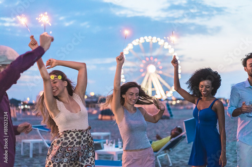 Canvas Print Happy friends making beach party after sunset with fireworks and drinking champa