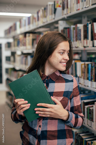 Young female girl student smiling with book in library 