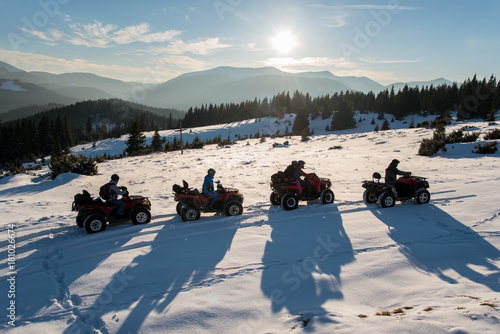 Group of people enjoying sunset, riding on quad bikes on snow in the the mountains in winter