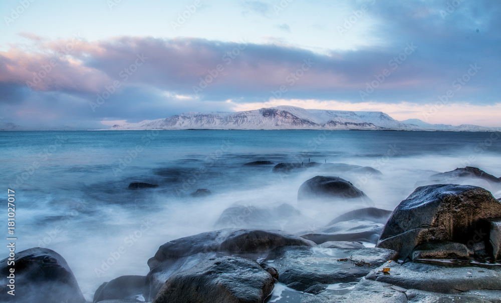Winter view of the mountains from the promenade. Reykjavik, Iceland. Coastline wet stones, washed by waves at sunset.
