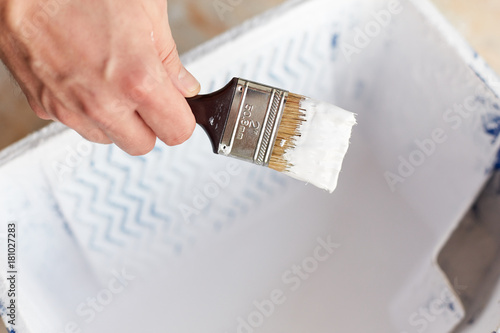 A bucket of white paint with a male hand holding a brush