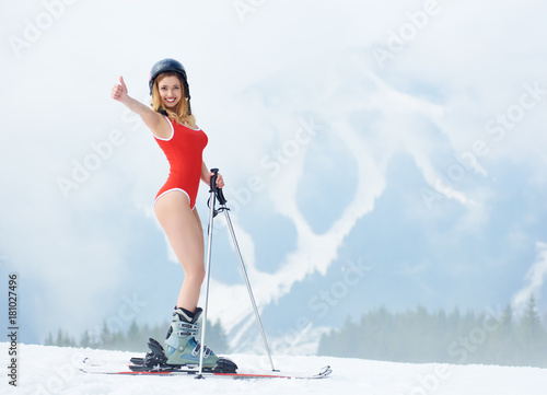 Картината върху платно Happy woman skier wearing red bodice, skis and helmet, showing thumbs up, standing on snowy slope at winter ski resort