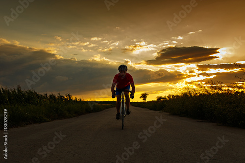 Silhouette of cyclist on road bike at sunset. Goes to camera.