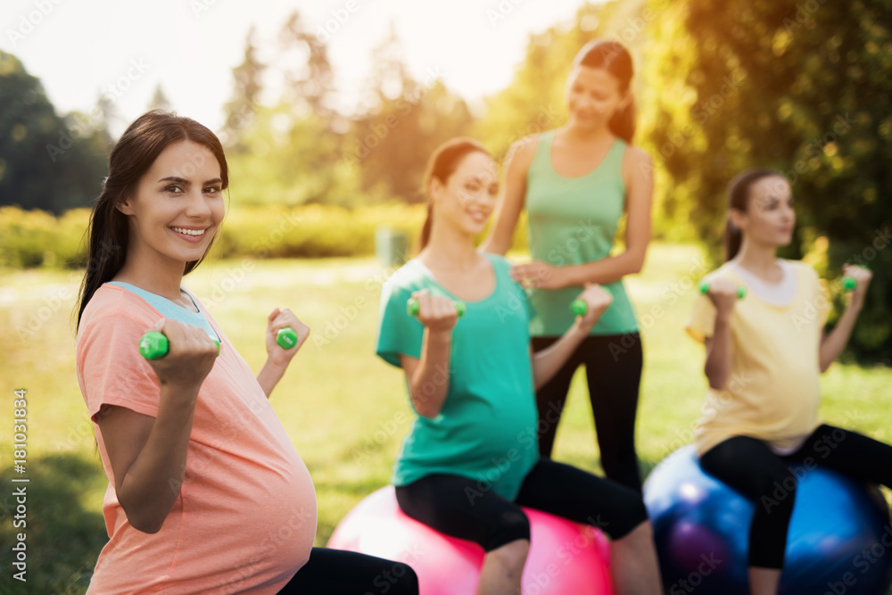Pregnancy yoga. Three pregnant women are engaged in fitness in the park. They sit on balls for yoga