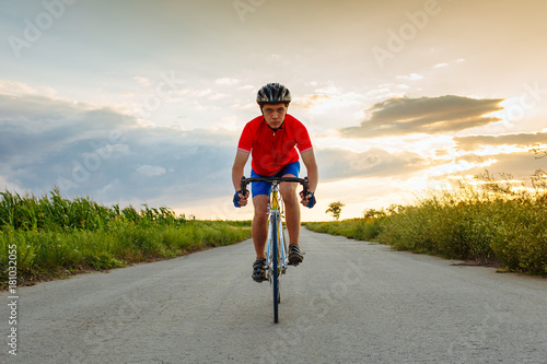 The cyclist in red blue form rides along fields of sunflowers. In background a beautiful blue sky.