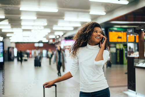 Obraz na plátně Woman traveller talking on phone in the airport terminal walkway with travel bag luggage