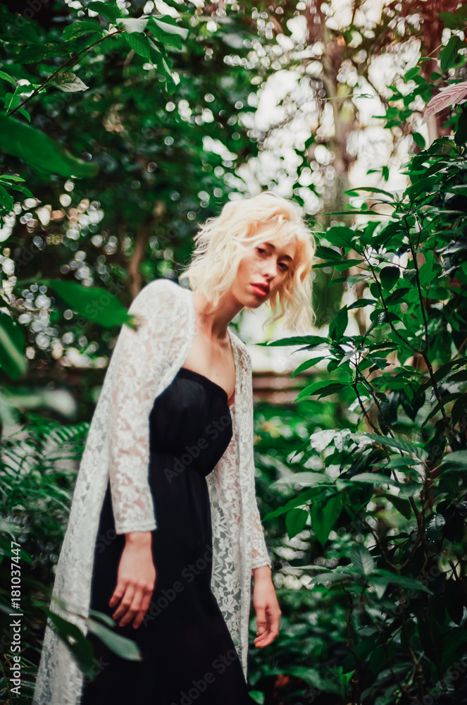 Fashion portrait of beautiful young with blonde hair and perfect figure posing in the palm leaves in the jungle. Scanned film with grain