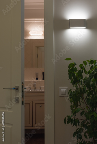 Wall LED lamps in the interior. Open white door to the bath