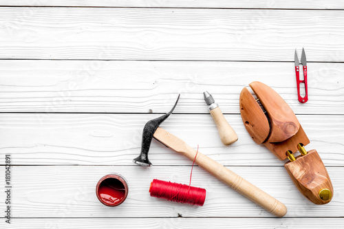 Shoe repair. Wooden last, hammer, awl, knife, thread on white wooden background top view copyspace