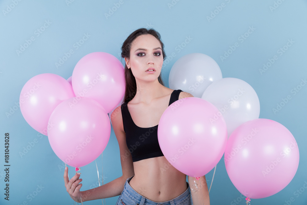 Brunette girl in jeans and a black top, surrounded by eight balloons