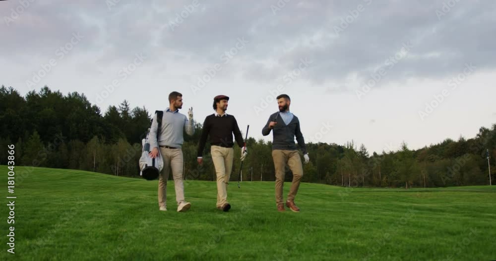 Attractive men walking with clubs on the golf field to start a game and talking on the nice sunny day. Outdoor Attractive men walking with clubs on the golf field to start a game and talking on the nice sunny day. Outdoor
