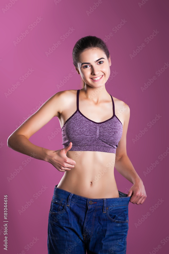 Fototapeta premium beautiful brunette girl shows her figure in big on her pants on a pink background