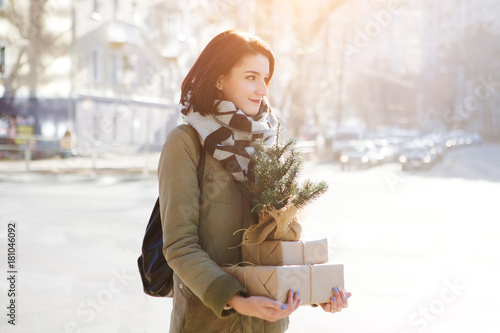 Outdoor portrait of beautiful happy smiling young woman with Christmas gifts on street.