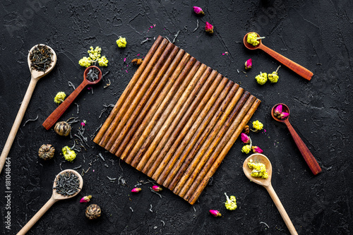 Aromatic tea. Wooden spoons with dried tea leaves, flowers and spices on black background top view mockup