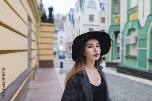Street portrait of a stylish woman on the background of the street of an old beautiful town. Beautiful girl in a hat stands on the background of a colored old architect