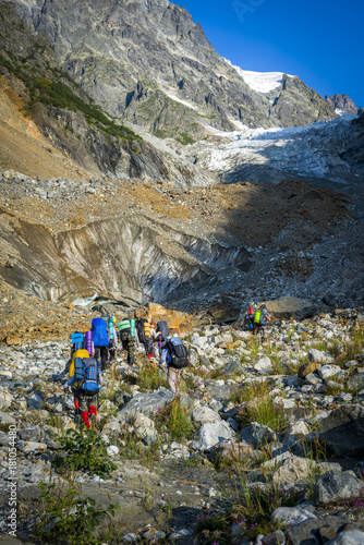 Tourists in the Caucasian Mountains. A group of tourists goes to a mountain pass on a stony slope and glacier.