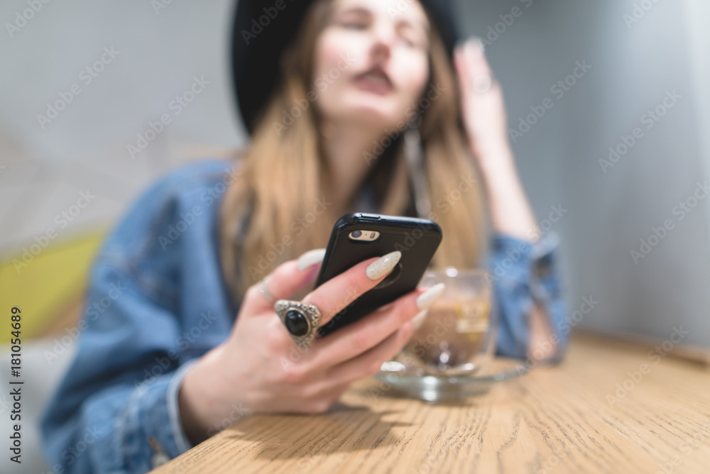 Hipster girl with a smearphone in her hands while lunch in a cozy cafe. Focus on your phone. Hipster girl with a smearphone in her hands while lunch in a cozy cafe. Focus on your phone.