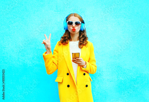 Fashion pretty woman with smartphone listens to music in headphones on a colorful blue background