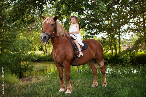 Llittle girl is riding a horse. Summer meadow.