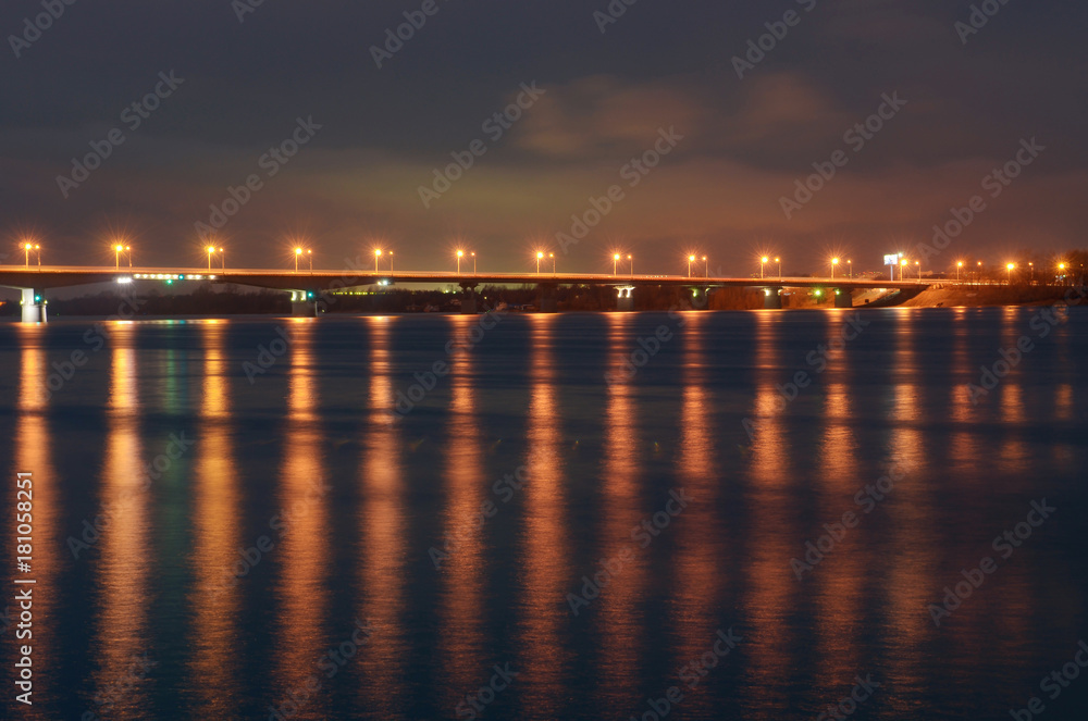 Night city embankment in Perm and bridge through the Kama river, lit by lanterns, the reflection of light in water.
