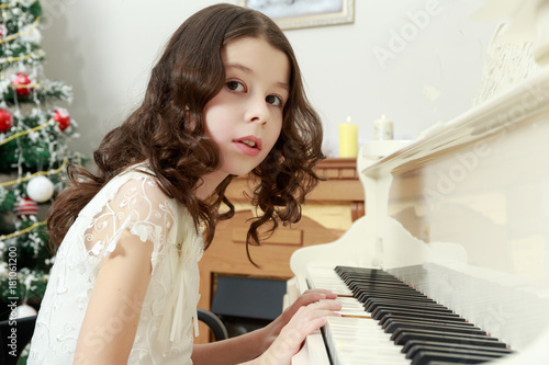 Beautiful girl in a white dress sitting at the piano.