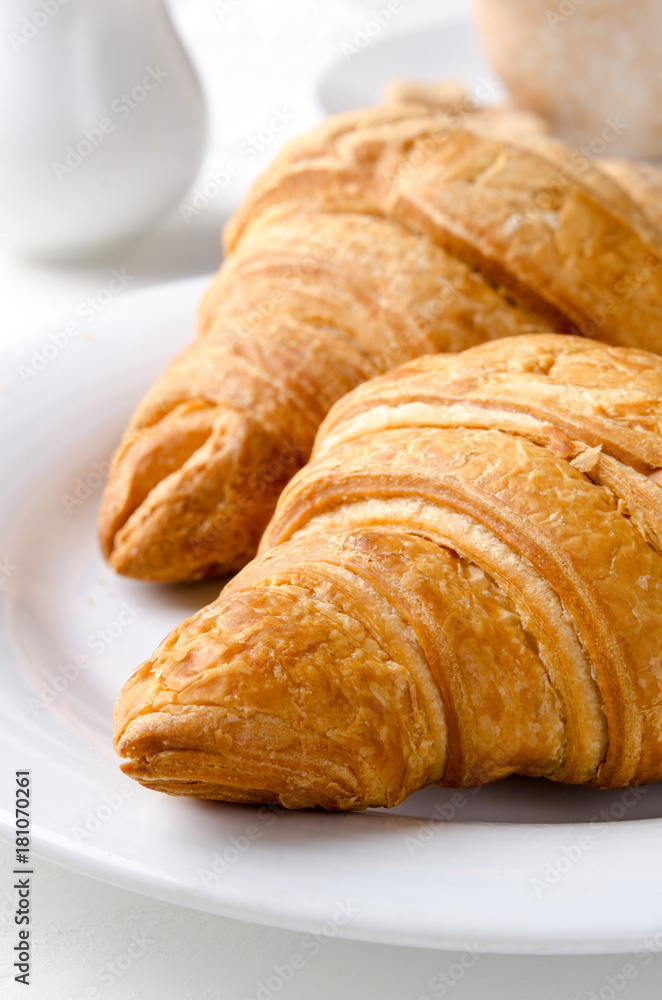 Traditional breakfast with fresh croissants and coffee on white wooden background.