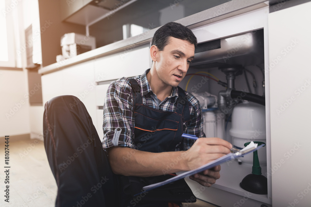 The plumber sits next to the kitchen sink on the floor and writes a report on the work done. The plumber sits next to the kitchen sink on the floor and writes a report on the work done.